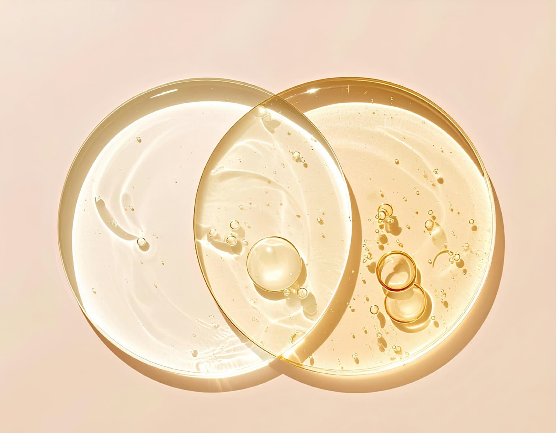 Three shallow glass dishes of skincare gel, cream and oil on a beige ground, one holding a single green leaf.