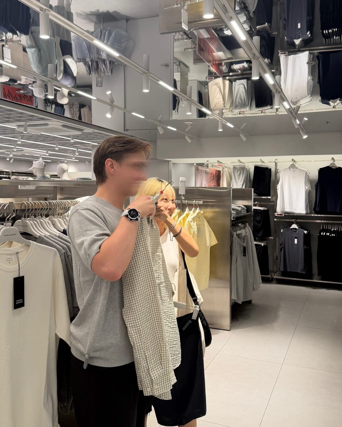 Eden holding a checked shirt up beside a client in a Seoul clothing store